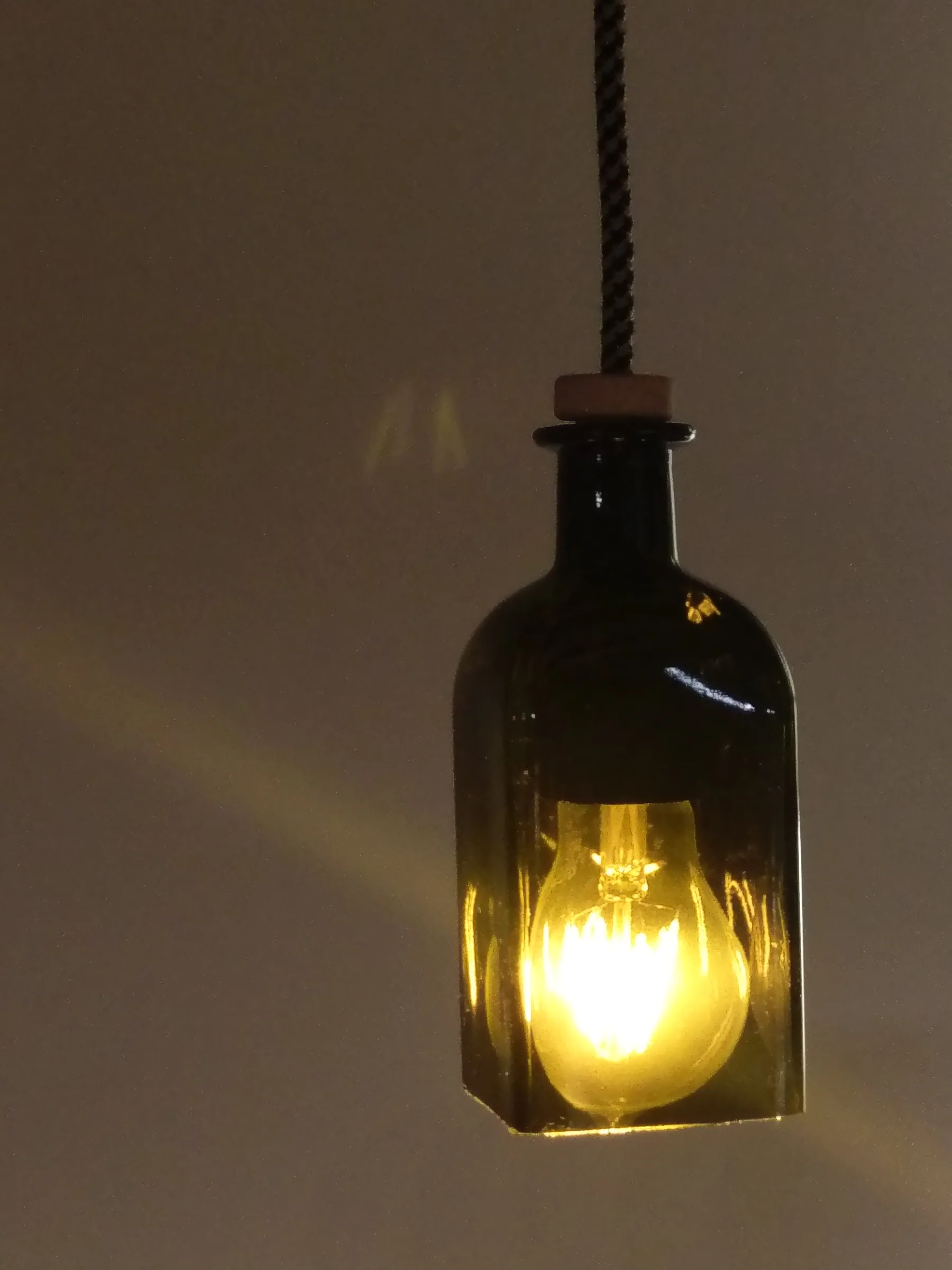 Green glass bottle used as a pendant lamp with a glowing filament bulb