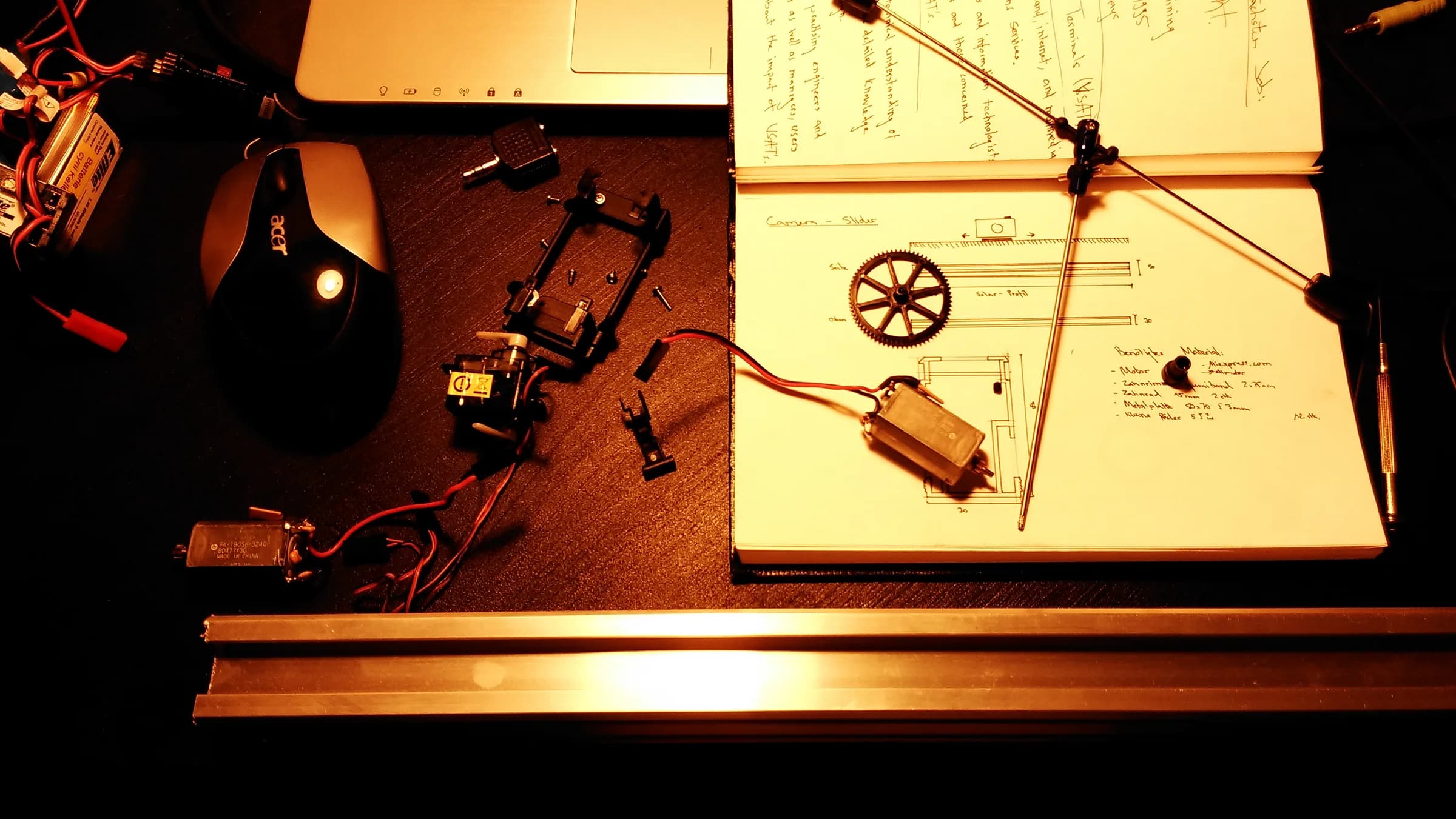 Workbench with a motor and wheel mechanism, a notebook and parts under warm light