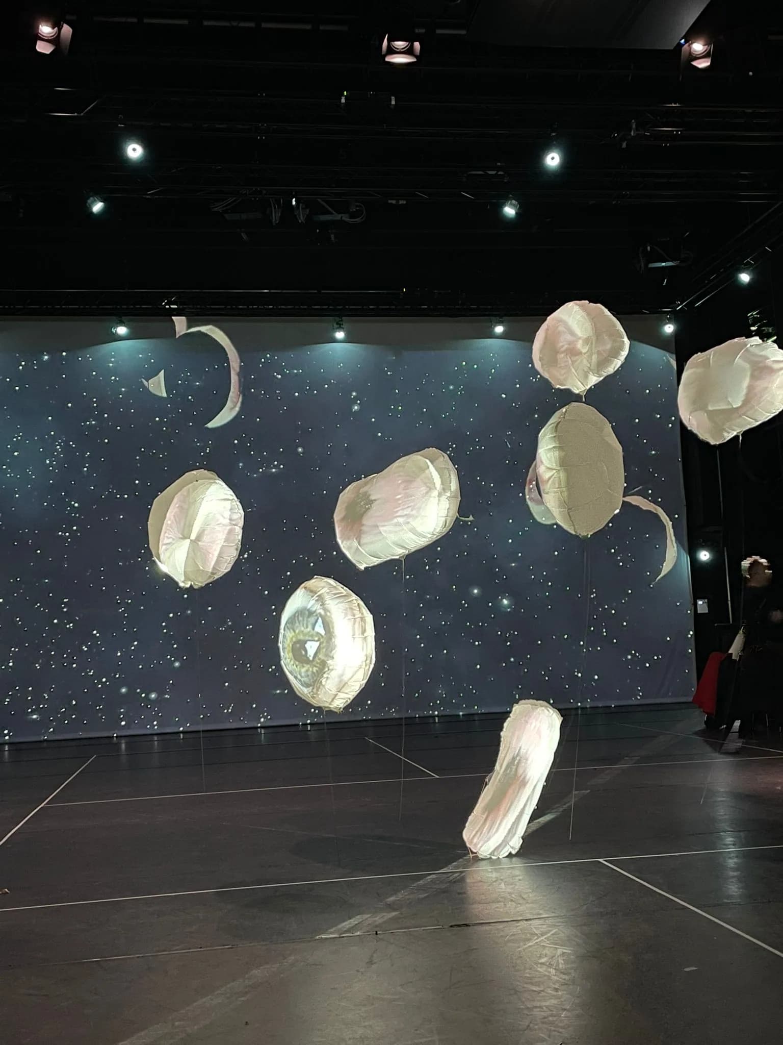 Stage installation with floating light objects carrying projected eyes in front of a starry projection