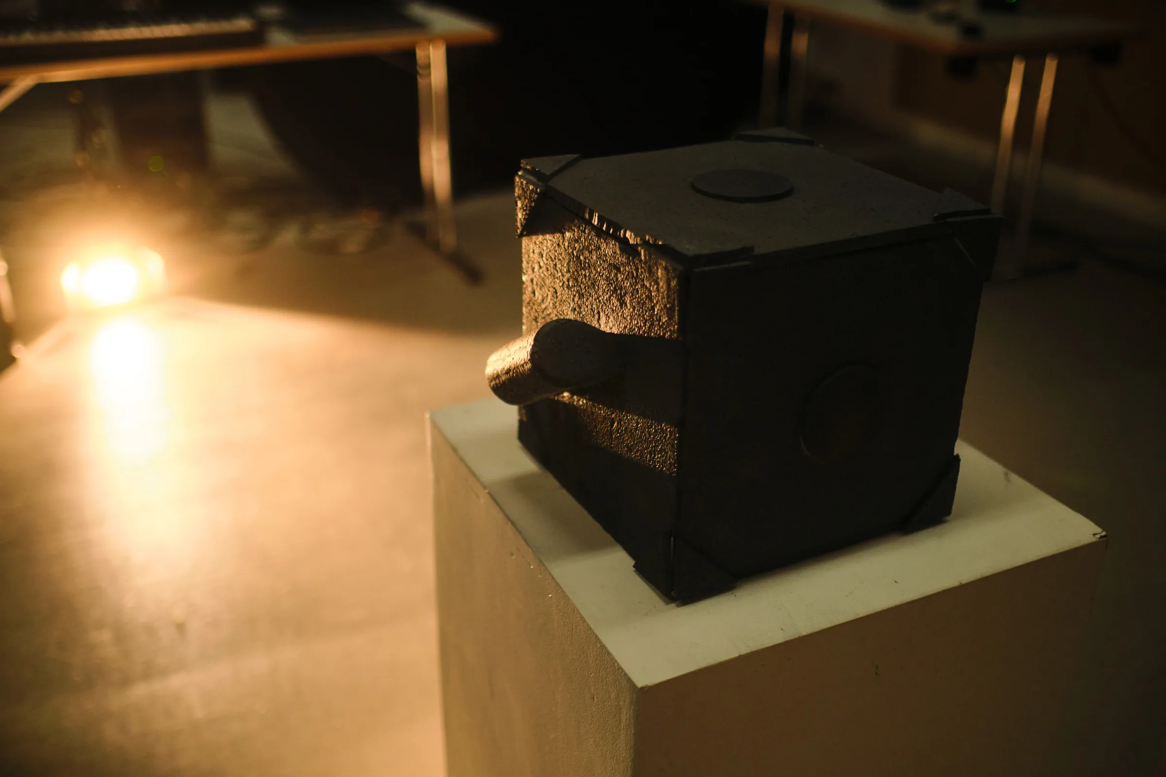 Gyro sound experiment: a black textured cube on a plinth in warm gallery light