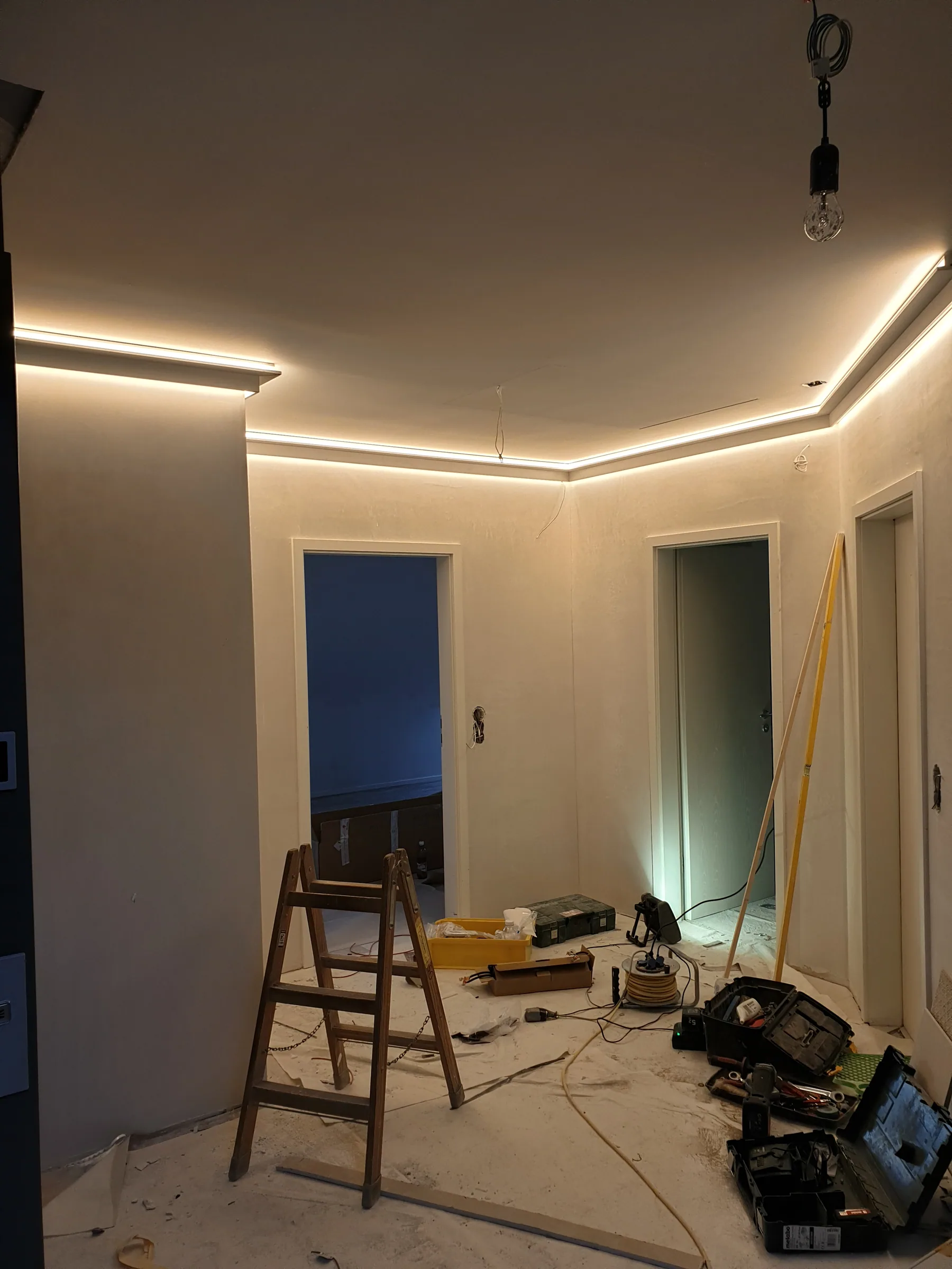 Hallway with warm LED cove lighting during construction, ladder and equipment on the floor
