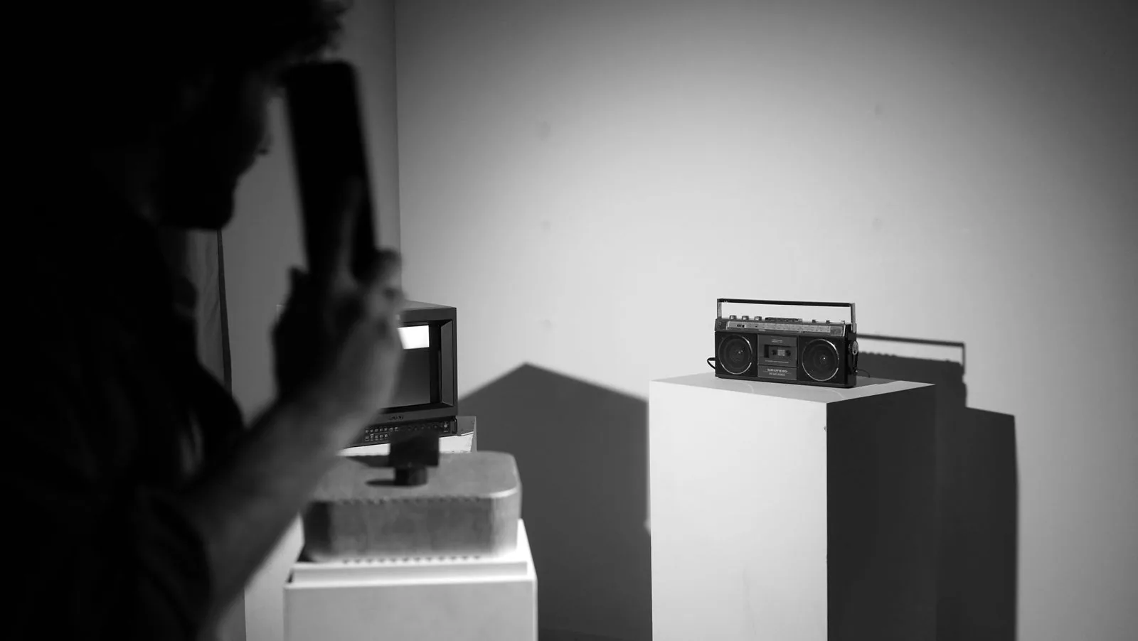 Person at a pedestal with a small screen and a boombox in a dim room