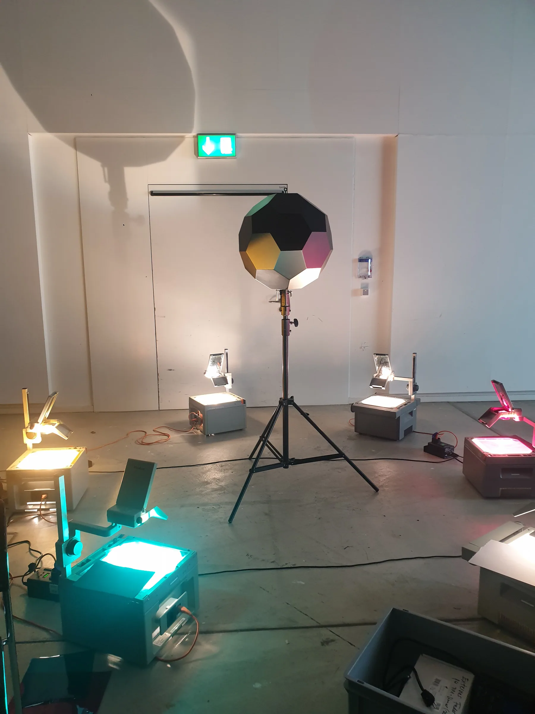 Experiments with overhead projectors: a faceted sphere on a tripod and colour-lit stage lights in an installation space