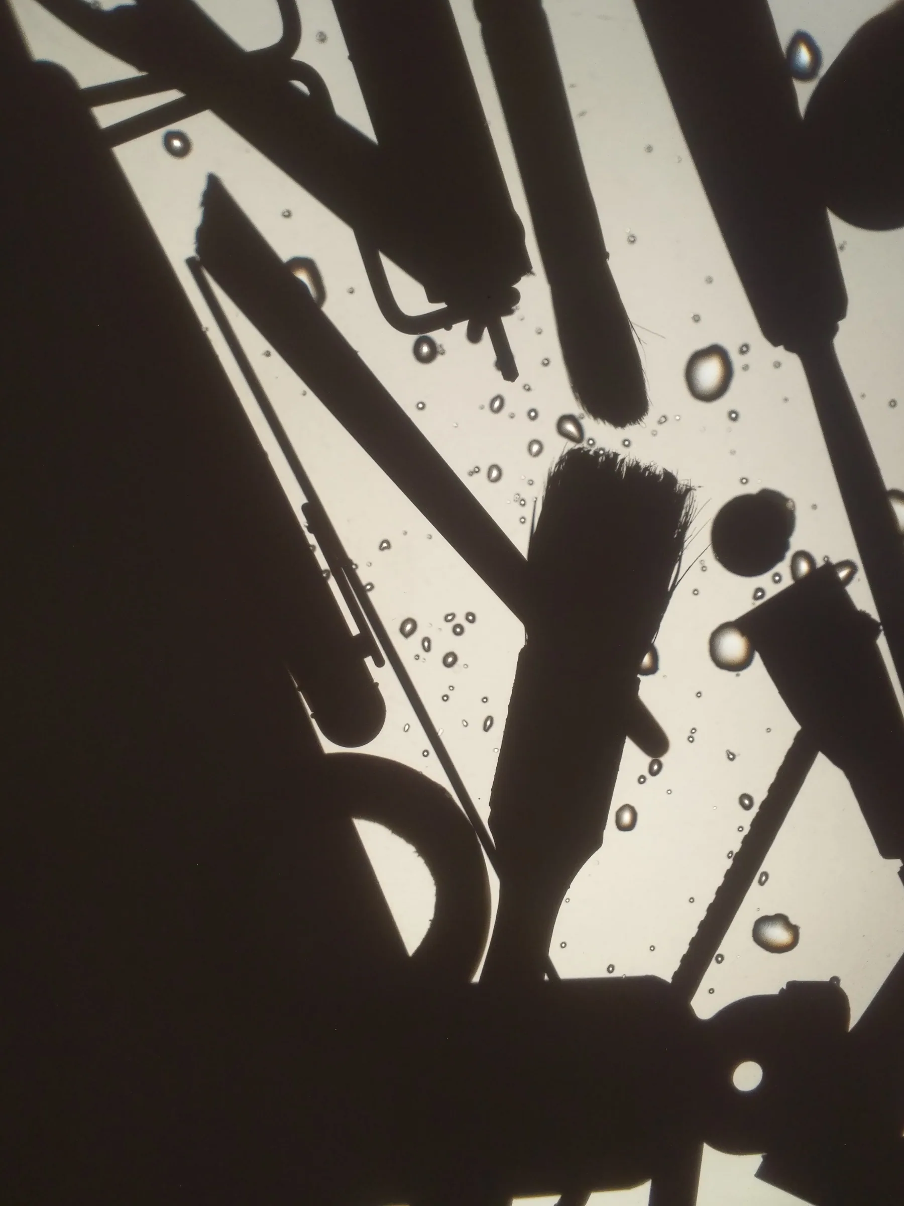 Dark tool-shaped silhouettes and water droplets on a backlit surface