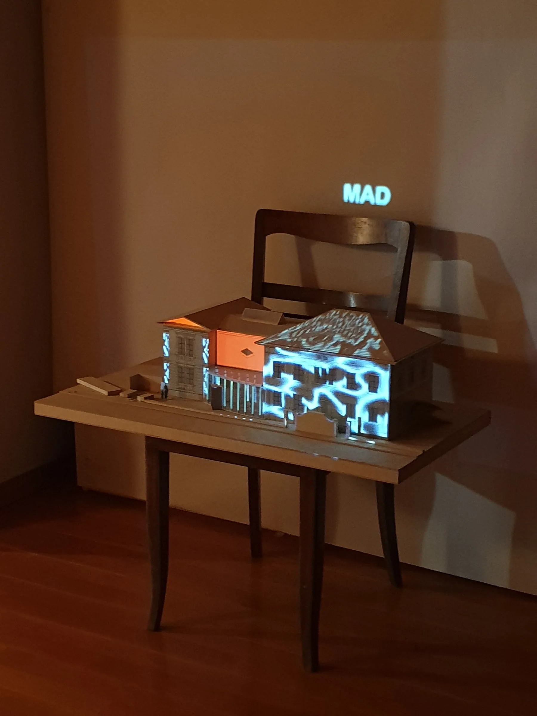 Miniature model of Villa Flora on a wooden table, projection-mapped with glowing blue and orange light